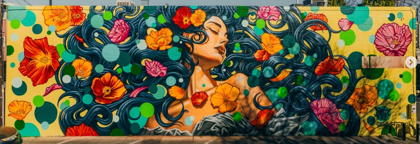 Panoramic vibrant mural by Matley Hurd in downtown San Jose featuring a woman looking upward surrounded by colorful poppies, peonies, turquoise leaves, and flowing hair.
