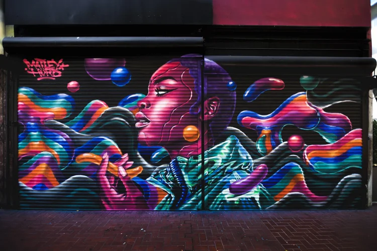 Vibrant mural on a corrugated metal door featuring a woman in profile surrounded by dynamic, 3D-like abstract flowing shapes in neon colors.