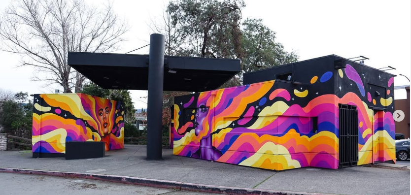 Vibrant mural on a bus depot in Napa CAfeaturing Matley Hurd's 'Star Goddess' characters and flowing abstract waves in sunset colors on a dark background.